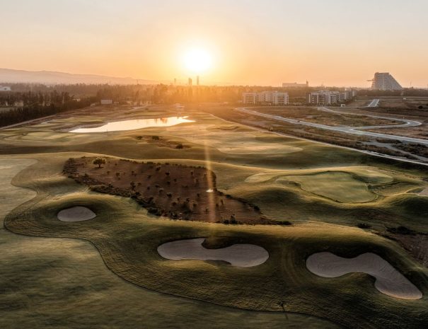 Limassol Greens aerial view of bunkers and fairways at sunrise, with the Limassol skyline